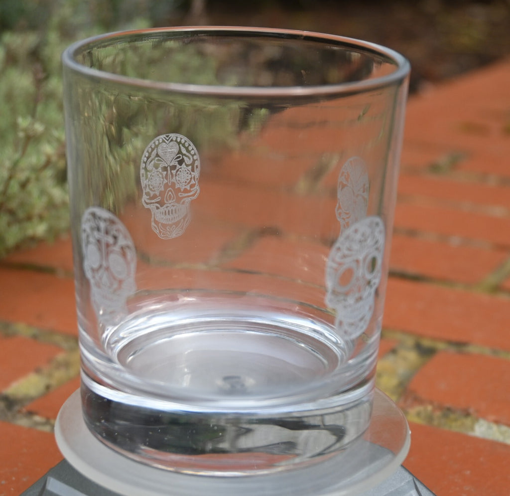 Four sugar skulls engraved around a glass tumbler for Day of the Dead